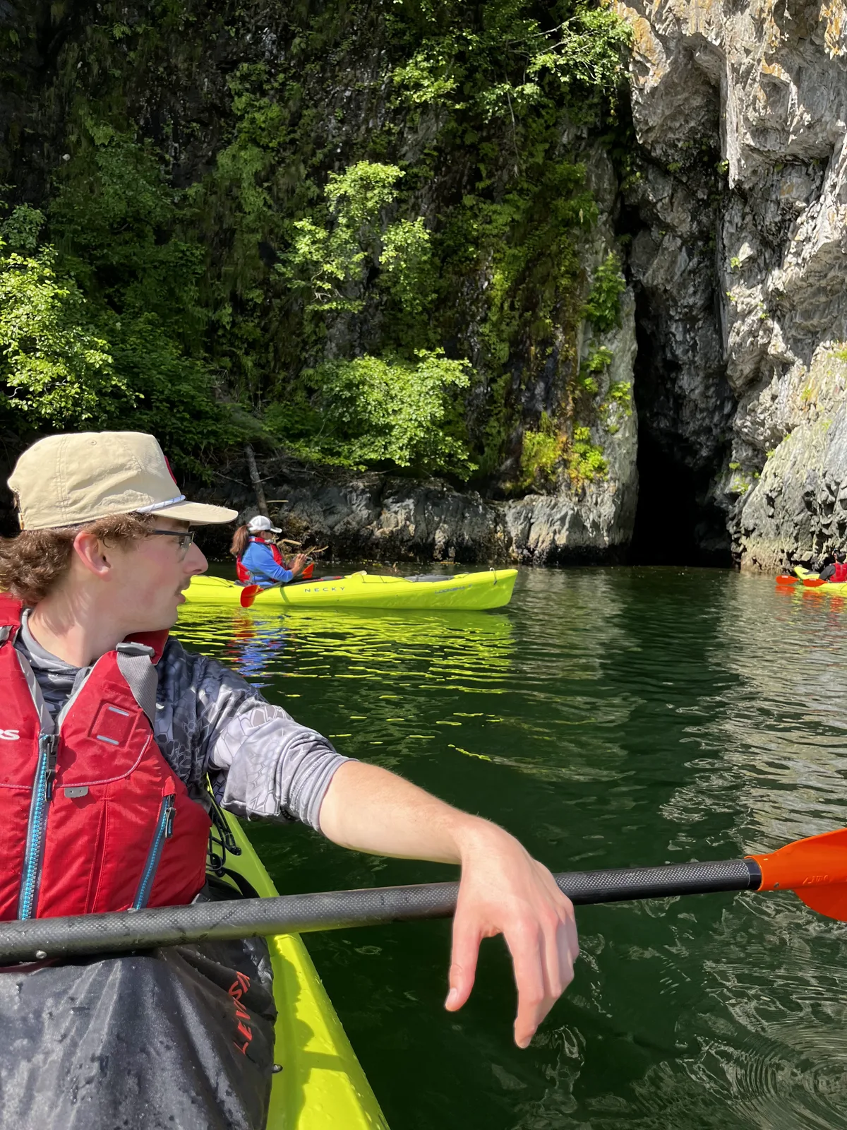 Guests kayaking past a moss-covered rock cliff and cave along the Sitka shoreline