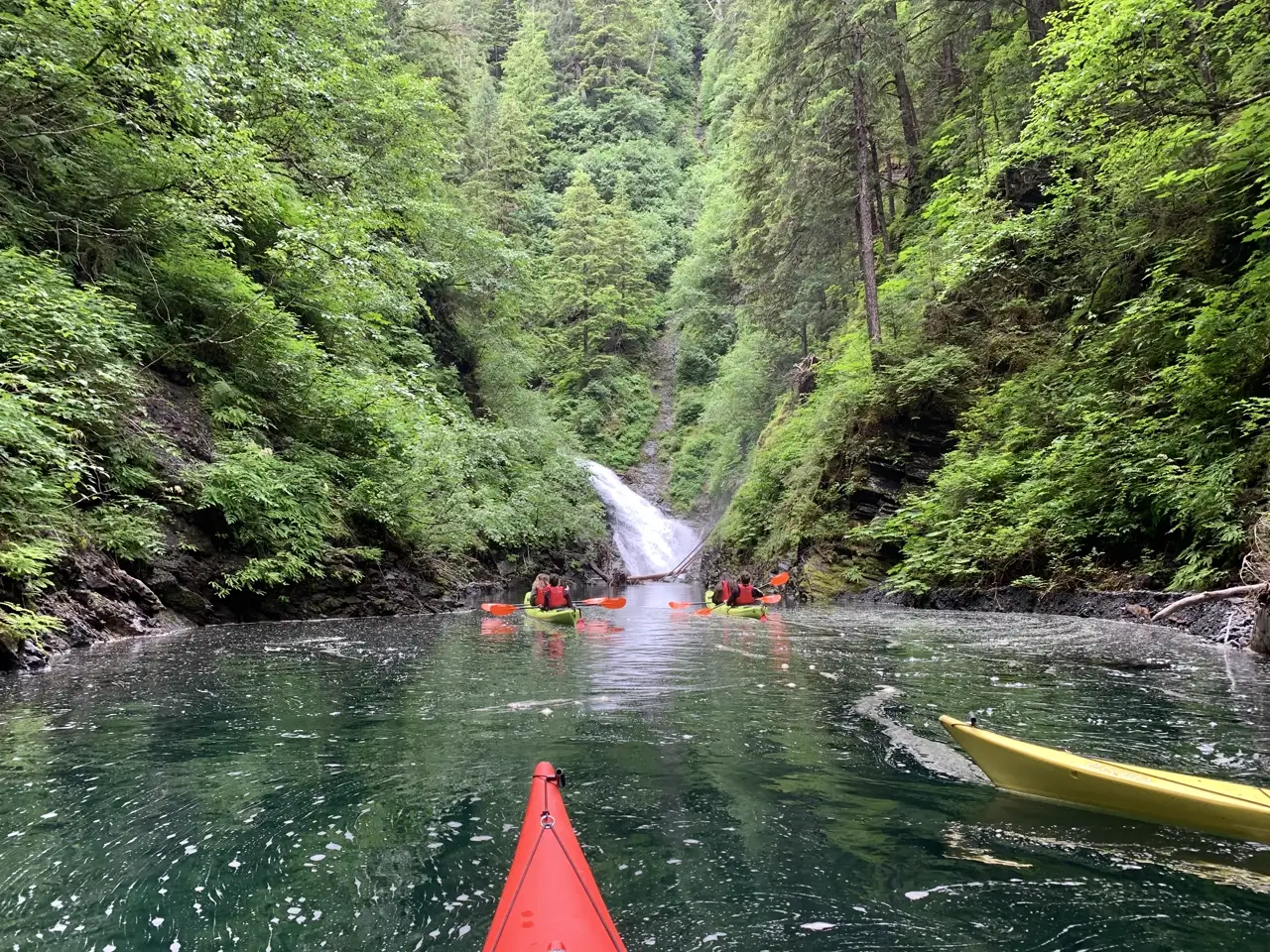 Kayakers approaching a waterfall on Blue Lake in the Tongass National Forest near Sitka, Alaska