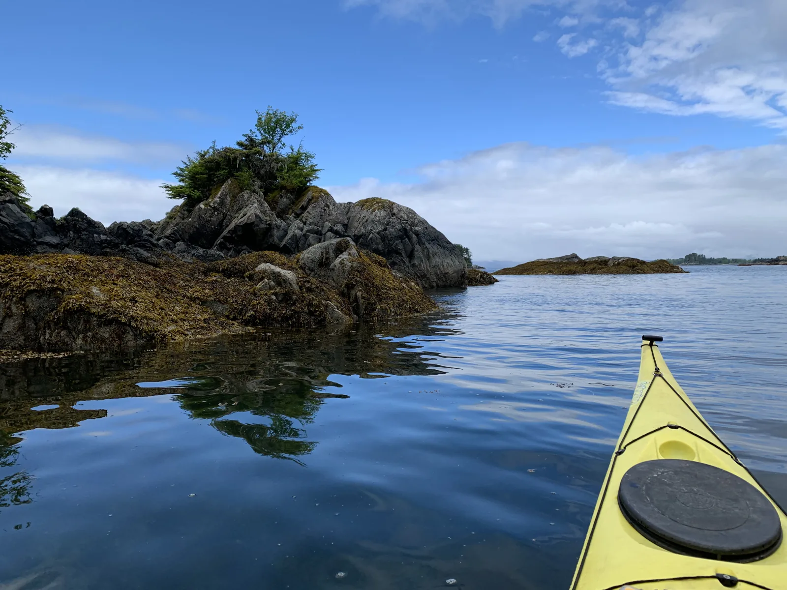 Kayak gliding past a rocky, tree-topped islet on the calm waters of Sitka Sound, Alaska